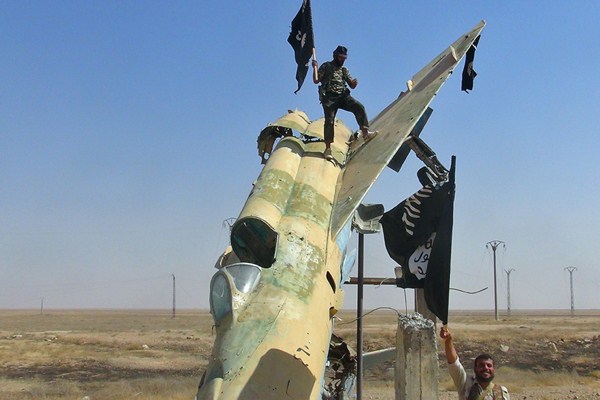 Fighters of the Islamic State waving the group's flag from a damaged display of a government fighter jet following the battle for the Tabqa air base, Raqqa, Syria, photo post Aug. 27, 2014 (AP photo/ Raqqa Media Center of the Islamic State group).