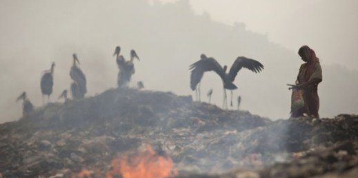 Smoke rises from burning garbage as an Indian woman looks for recyclable material at a dumping site on the outskirts of Gauhati, India, Nov. 14, 2014 (AP photo by Anupam Nath).