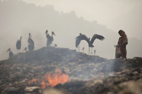 Smoke rises from burning garbage as an Indian woman looks for recyclable material at a dumping site on the outskirts of Gauhati, India, Nov. 14, 2014 (AP photo by Anupam Nath).