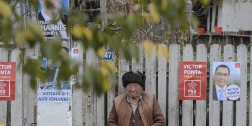 An elderly man surrounded by campaign posters sits on a bench in front of his home in Floroaica village, Calarasi county, Romania. Nov. 11, 2014 (AP photo by Octav Ganea, Mediafax).