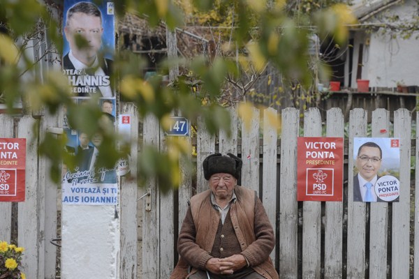 An elderly man surrounded by campaign posters sits on a bench in front of his home in Floroaica village, Calarasi county, Romania. Nov. 11, 2014 (AP photo by Octav Ganea, Mediafax).