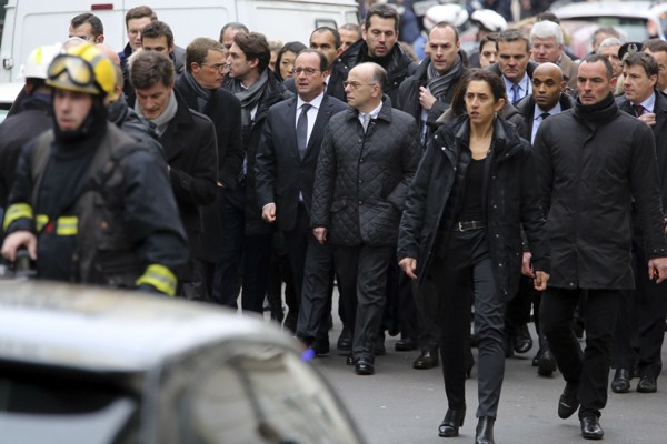 French President Francois Hollande, center left, flanked by French Interior Minister Bernard Cazeneuve, right, walks outside the French satirical newspaper Charlie Hebdo’s office, in Paris, Jan. 7, 2015 (AP photo by Remy De La Mauviniere).