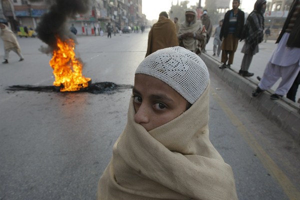 A Pakistani religious student stands before a fire set by protesters demanding the government unmask culprits of the Taliban attack on a school, Peshawar, Pakistan, Dec. 16, 2014 (AP photo by Mohammad Sajjad).