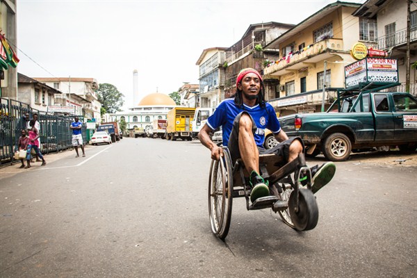 A man travels along a street in his wheelchair during a three-day lockdown to prevent the spread on the Ebola virus, Freetown, Sierra Leone, Sept. 21, 2014 (AP photo by Michael Duff).