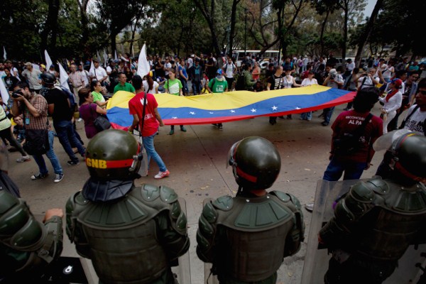 Opposition demonstrators display a Venezuelan flag in front of a line of Bolivarian National Guard officers dressed in riot gear in Caracas, Venezuela, Feb. 12, 2015 (AP photo by Fernando Llano).