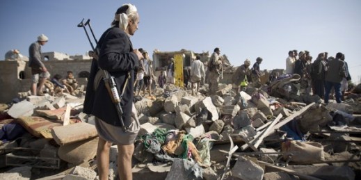 A Houthi fighter stands guard as people search for survivors under the rubble of houses destroyed by Saudi airstrikes near Sanaa Airport, Yemen, March 26, 2015 (AP photo by Hani Mohammed).