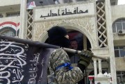 A fighter from Syria’s al-Qaida-linked Nusra Front holds his group’s flag as he stands in front of the governorate building in Idlib province, north Syria, March 28, 2015 (AP Photo/Nusra Front on Twitter).