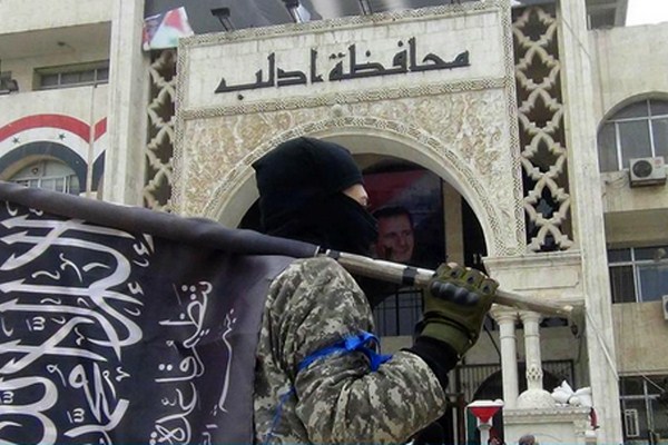 A fighter from Syria’s al-Qaida-linked Nusra Front holds his group’s flag as he stands in front of the governorate building in Idlib province, north Syria, March 28, 2015 (AP Photo/Nusra Front on Twitter).