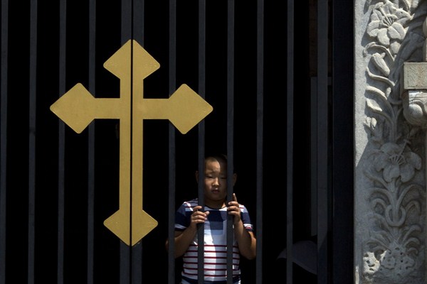 A child peers out near a cross on a gate of the Wangfujing Catholic Church, Beijing, China, Aug. 14, 2014 (AP photo by Ng Han Guan).