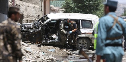 Afghan security personnel inspect a damaged vehicle at the site of a suicide attack that targeted a NATO convoy in Kabul, Afghanistan, July 7, 2015 (AP photo by Rahmat Gul).