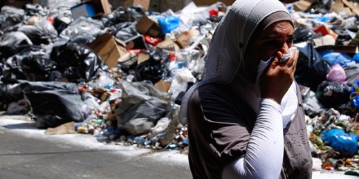 A Lebanese woman covers her nose from the smell as she walks on a street partly blocked by piles of garbage, Beirut, Lebanon, July 27, 2015 (AP photo by Hassan Ammar).