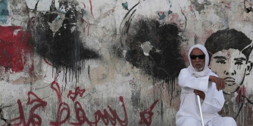 A Bahraini man sits on a street by a wall covered in political graffiti, which is regularly sprayed over by authorities and reapplied by government opponents, Malkiya, Bahrain,, June 11, 2015 (AP photo by Hasan Jamali).