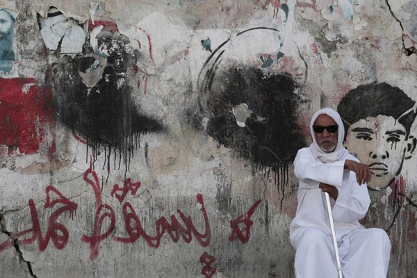 A Bahraini man sits on a street by a wall covered in political graffiti, which is regularly sprayed over by authorities and reapplied by government opponents, Malkiya, Bahrain,, June 11, 2015 (AP photo by Hasan Jamali).