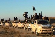 In this undated file photo, militants of the Islamic State group hold up their weapons and wave its flags on their vehicles in a convoy on a road leading to Iraq from Raqqa, Syria (Militant website via AP).