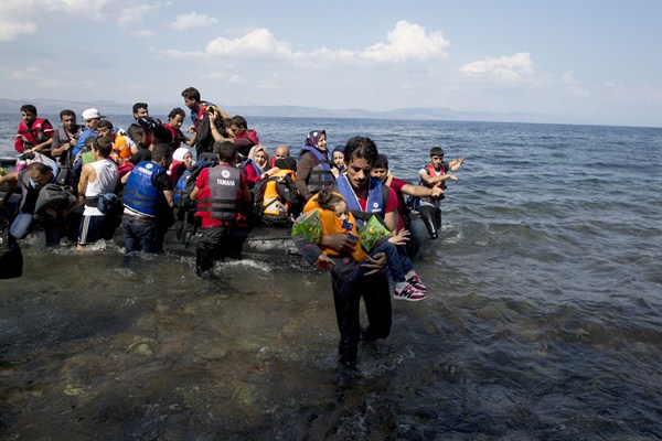 A man carries a child as migrants and refugees arrive on a dinghy after crossing from Turkey to Lesbos, Greece, Sept. 8, 2015 (AP photo by Petros Giannakouris).