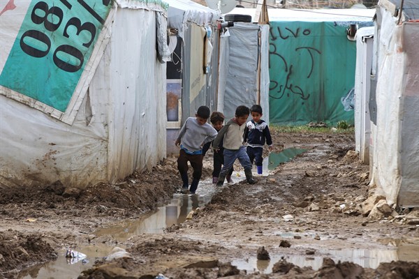 Syrian boys walk between tents in mud from the heavy rains at a refugee camp in the town of Marej in the Bekaa valley, east Lebanon, Feb. 25, 2015 (AP photo by Hussein Malla).
