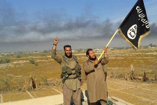 An Islamic State militant waves his group's flag as he and another celebrate in Fallujah, Iraq, photo released, June 28, 2015 (Militant website via AP).