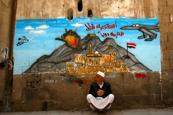 An elderly man sits under a mural depicting a Saudi-led airstrike hitting Sanaa with Arabic writing that reads, "using internationally banned bombs," in the Old City of Sanaa, Yemen, Sept. 19, 2015 (AP photo by Hani Mohammed).