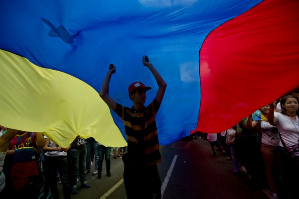 An opposition member walks under a Venezuelan flag during a rally in Caracas, Venezuela, Sept. 19, 2015 (AP photo by Fernando Llano).