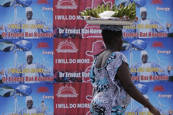 A banana seller walks past election posters, Freetown, Sierra Leone, Nov. 19, 2012 (AP photo by Rebecca Blackwell).
