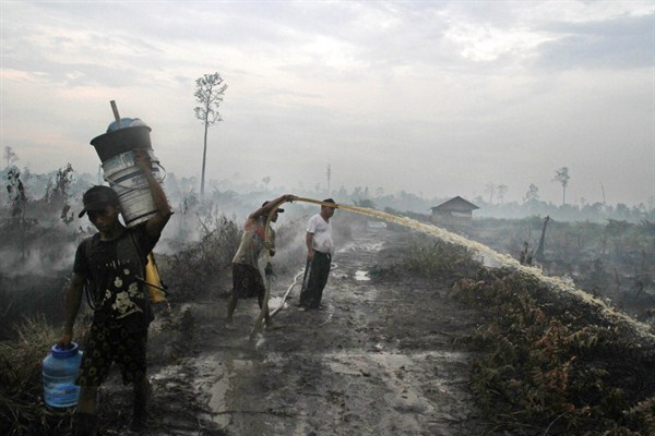 A man sprays water in an attempt to extinguish bush fires on a peat land, Siak, Indonesia, March 17, 2014 (AP photo by Rony Muharrman).