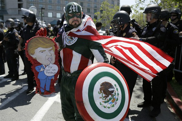 Erik Lopez, dressed as "Captain Mexico," stands in front of police officers while protesting Republican presidential candidate Donald Trump, Burlingame, California, April 29, 2016 (AP photo by Eric Risberg).