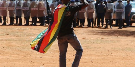 A man wearing a Zimbabwean flag salutes riot police during a protest, Harare, Zimbabwe, Aug. 26, 2016 (AP photo).