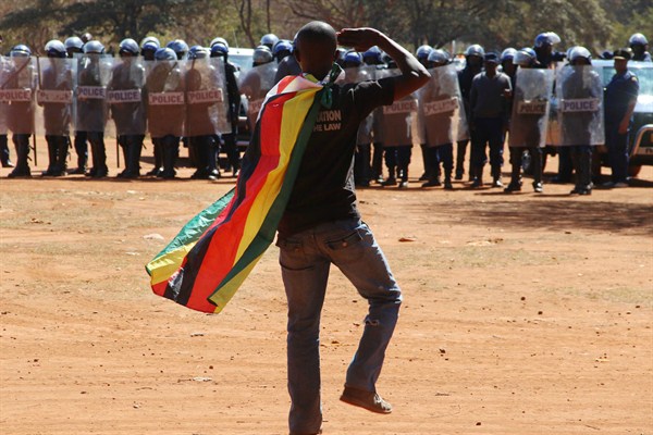 A man wearing a Zimbabwean flag salutes riot police during a protest, Harare, Zimbabwe, Aug. 26, 2016 (AP photo).