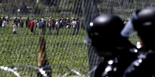 Macedonian police officers look as migrants gather to protest from the Greek side of the border fence between Macedonia and Greece, April 13, 2016 (AP photo by Boris Grdanoski).