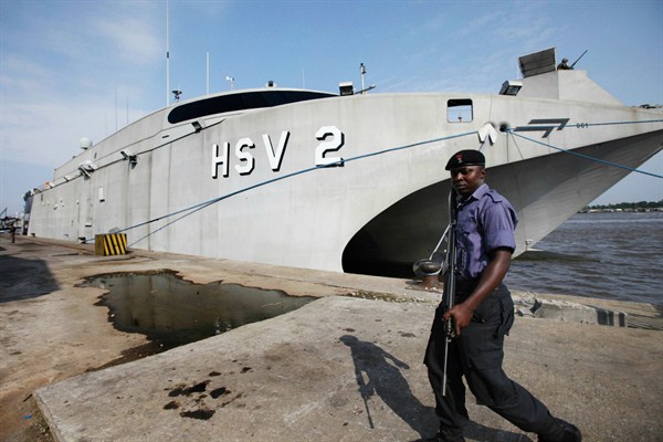A Nigerian Naval officer walks past a U.S. high-speed vessel, Lagos, Nigeria, Aug. 9, 2011 (AP photo by Sunday Alamba).