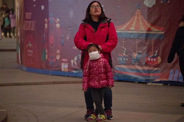A woman helps a child wear a mask to protect against air pollution, Beijing, China, Nov. 26, 2016 (AP photo by Ng Han Guan).