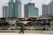 A woman walks by a slum in front of an apartment construction site, Jakarta, Indonesia, Aug. 14, 2014 (AP photo photo Tatan Syuflana).