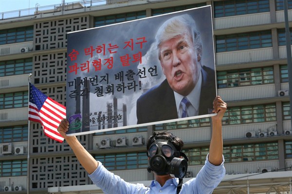 A South Korean environmental activist wearing a gas mask and bearing a sign denouncing the U.S. withdrawal from the Paris climate accord participates in a protest in front of the U.S. Embassy, Seoul, June 5, 2017 (AP photo by Ahn Young-joon).