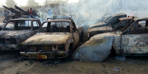 People stand behind burned-out cars after a suicide bombing in Maiduguri, northeastern Nigeria, Feb. 17, 2017 (AP photo by Hamza Suleiman).