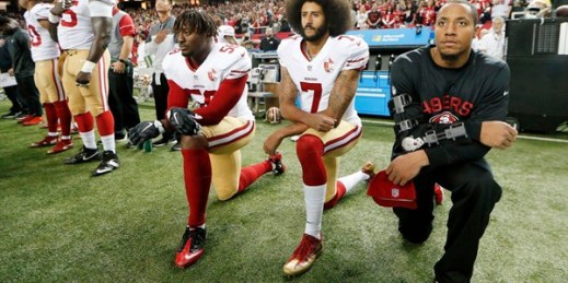 Former San Francisco 49ers quarterback Colin Kaepernick, middle, and teammate Eli Harold, left, kneel during the playing of the national anthem before an NFL football game, Atlanta, Georgia, Dec. 18, 2016 (AP photo by John Bazemore).