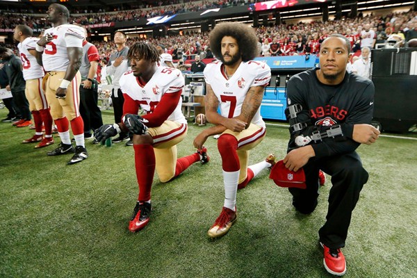 Former San Francisco 49ers quarterback Colin Kaepernick, middle, and teammate Eli Harold, left, kneel during the playing of the national anthem before an NFL football game, Atlanta, Georgia, Dec. 18, 2016 (AP photo by John Bazemore).