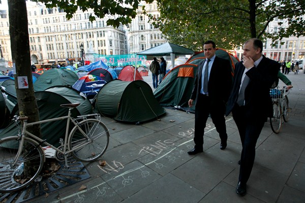 Businessmen walk past tents put up by protesters from the Occupy London Stock Exchange group outside St Paul's Cathedral, London, Oct. 17, 2011 (AP photo by Matt Dunham).