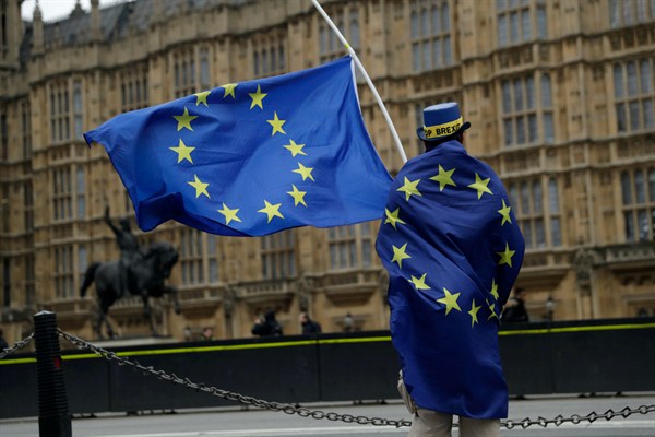 A Pro-EU membership supporter holds European Union flags as he protests against Brexit across the street from the Houses of Parliament, London, Dec. 5, 2017 (AP photo by Matt Dunham).