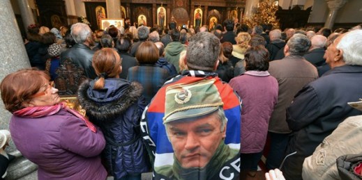 A man wrapped in a flag adorned with a photo of former Bosnian Serb military leader Ratko Mladic prays in a church as part of ceremonies to celebrate a banned Serb holiday, Banja Luka, Bosnia, Jan. 9, 2018 (AP photo by Radivoje Pavicic).