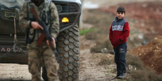 A child looks on as a fighter with the Free Syrian Army secures a checkpoint on the outskirts of Azaz, Syria, Jan. 27, 2018 (AP photo by Lefteris Pitarakis).