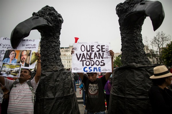 A man flanked by two large representations of vultures holds a sign that reads, in Spanish, “Let them all go” during a protest against Peru’s political class, Lima, March 22, 2018 (AP photo by Rodrigo Abd).