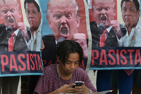 A demonstrator checks his smart phone in front of pictures of U.S. President Donald Trump and Philippine President Rodrigo Duterte, Manila, Philippines, Nov. 14, 2017 (AP photo by Aaron Favila).