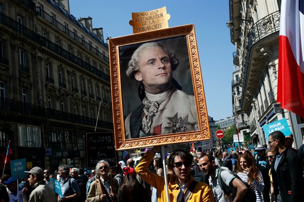 A protester carries a picture of French President Emmanuel Macron depicted as King Louis XVI, Paris, France, May 5, 2018 (AP photo by Francois Mori).