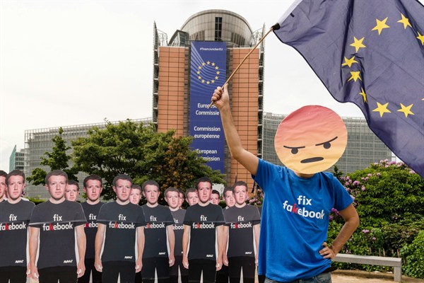 A demonstrator waves the European flag as he stands next to life-sized Mark Zuckerberg cutouts to protest against fake Facebook accounts spreading disinformation, Brussels, May 22, 2018 (AP photo by Geert Vanden Wijngaert).