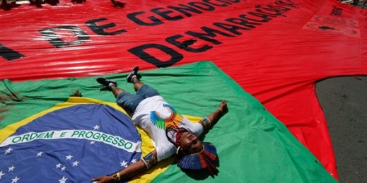 An indigenous man lies on top of a Brazilian flag representing indigenous people who were killed fighting for their land, Brasilia, Brazil, April 26, 2018 (AP photo by Eraldo Peres).