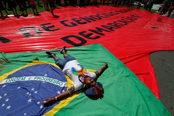 An indigenous man lies on top of a Brazilian flag representing indigenous people who were killed fighting for their land, Brasilia, Brazil, April 26, 2018 (AP photo by Eraldo Peres).