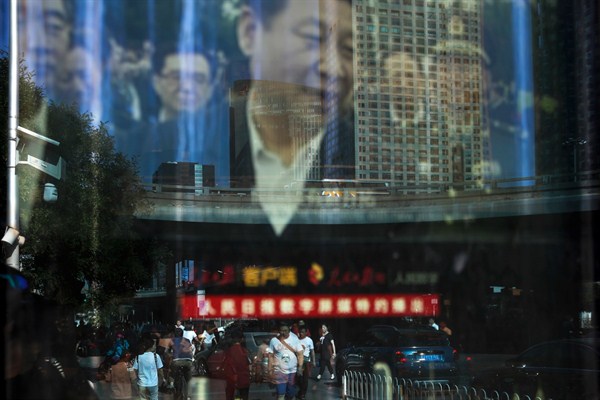 People and motorists are reflected on an electronic display panel showing video footage of Chinese President Xi Jinping near the central business district of Beijing, China, May 30, 2018 (AP photo by Andy Wong).