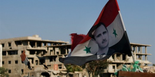 A Syrian national flag with the picture of the President Bashar al-Assad hangs at an army checkpoint in the town of Douma in the eastern Ghouta region outside Damascus, July 15, 2018 (AP photo by Hassan Ammar).