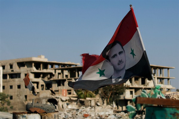 A Syrian national flag with the picture of the President Bashar al-Assad hangs at an army checkpoint in the town of Douma in the eastern Ghouta region outside Damascus, July 15, 2018 (AP photo by Hassan Ammar).