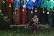 A Bhutanese child sits as adults in traditional costume stand in a queue to cast their votes for the nation’s parliamentary election outside a polling station at Rikhey, Bhutan, April 23, 2013 (AP photo by Anupam Nath).